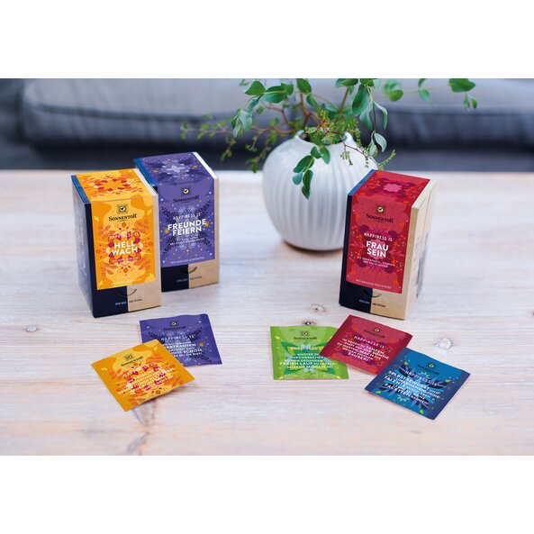 Zu sehen sind sind drei Happiness Is Doppelkammerpackungen und weitere einzelne Tees. 