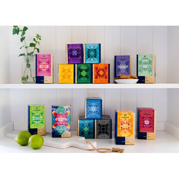 Zu sehen sind alle Happiness Is Sorten. Die Tee Packungen stehen in einem Regal auf zwei Ebenen.
